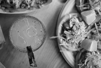 Black and white image of margarita next to a plate of tacos